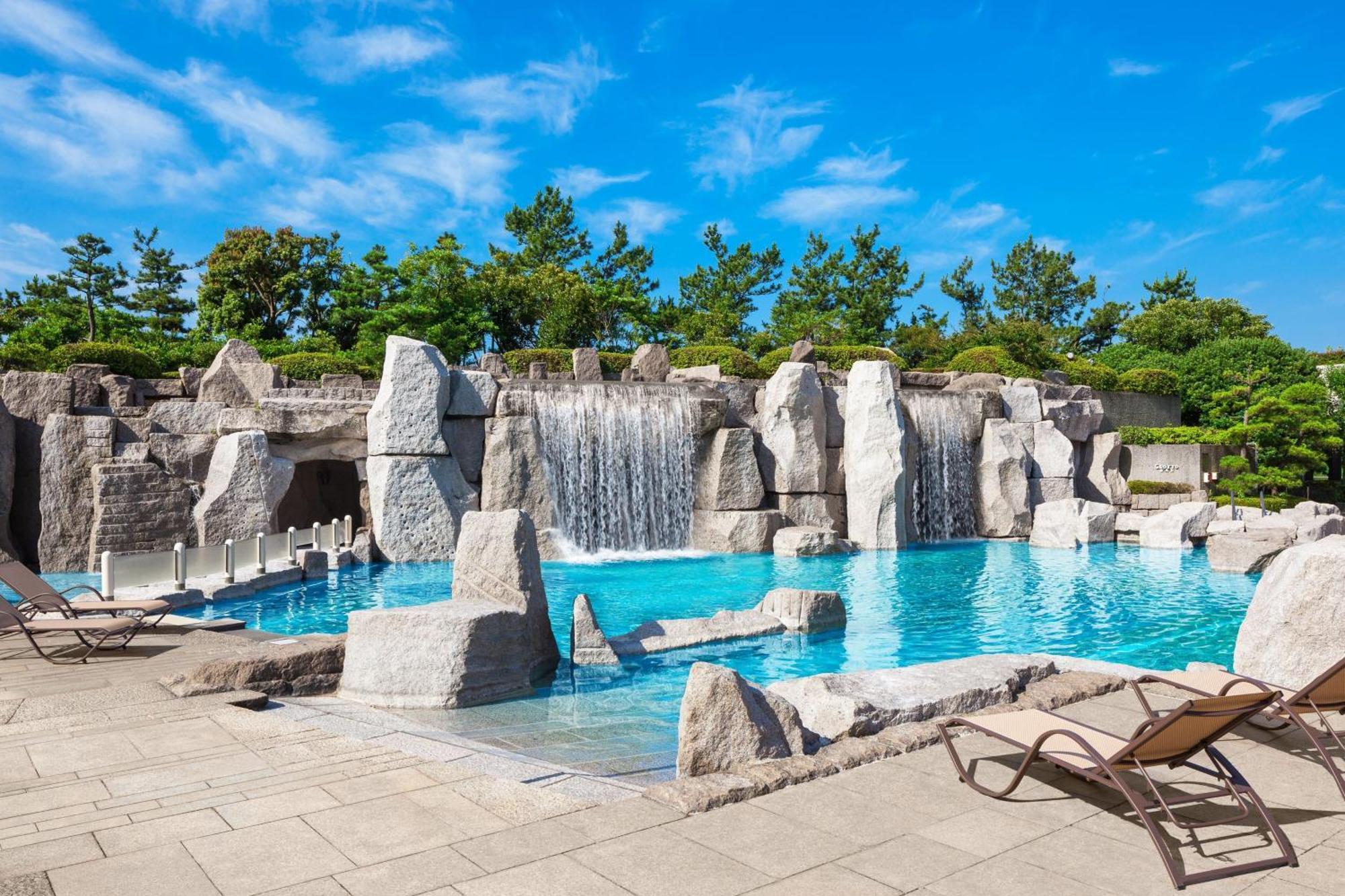 Sheraton Grande Tokyo Bay Hotel Urayasu Exterior photo The photo showcases a beautiful outdoor pool area surrounded by natural rock formations. There are several sand-colored stone structures, some of which feature water cascading down them, creating small waterfalls. The crystal-clear water of the pool 